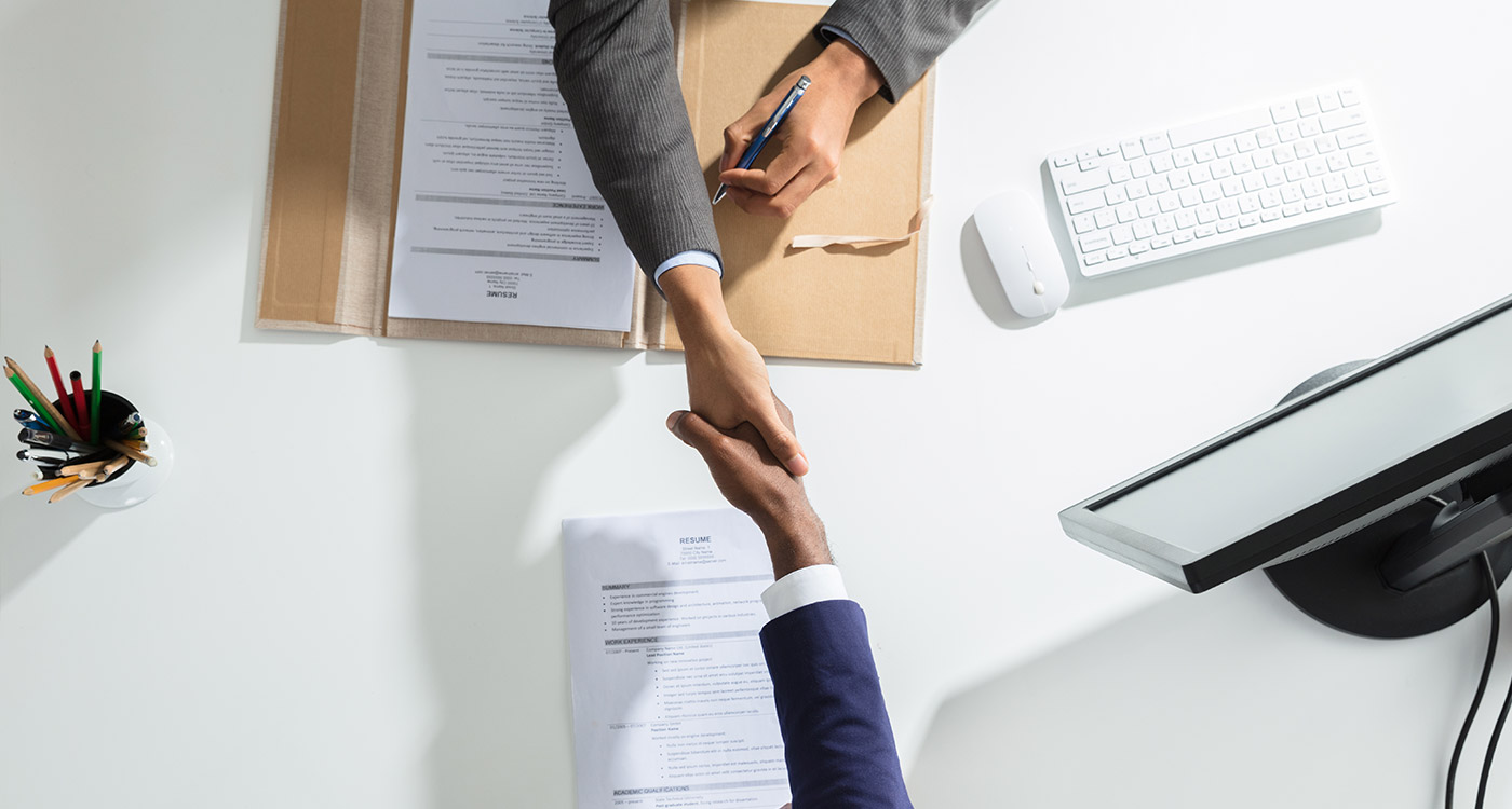 High Angle View Of Businessperson Shaking Hand With Candidate Over White Desk